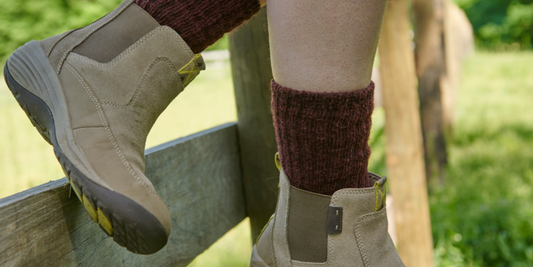 A person wearing work boots and red alpaca crew socks sits on an oak fenceline