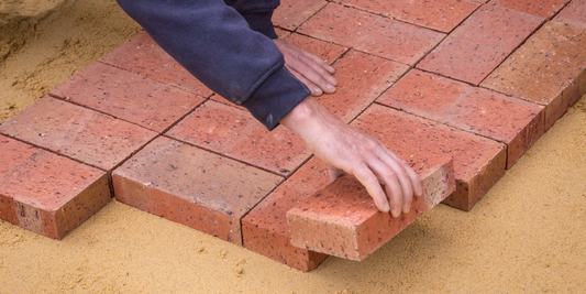 A person is setting down a brick as they create a brick walkway