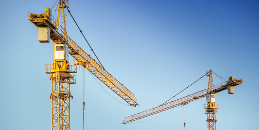 The tops of two cranes are seen with a blue sky background.