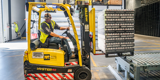 Man is looking backwards while operating a forklift with a bunch of pallets on it.