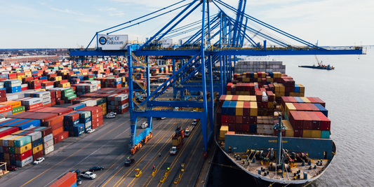 A cargo ship with a bunch of colorful containers on it is docked at a dock with a ton of cargo ready to be placed on the ship.