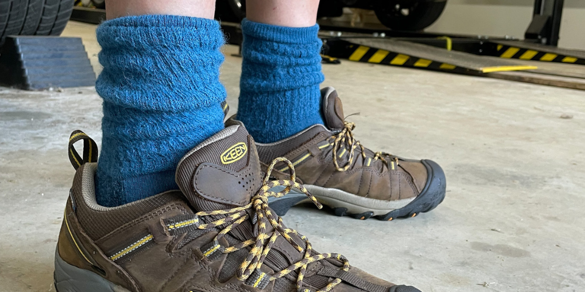 Blue alpaca crew socks are being worn in a brown pair of work boots in a garage