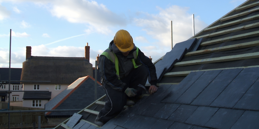 A man in construction vest and hard hat puts tile on a roof.