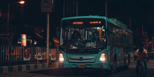 A blue bus drives through a city street at night time.