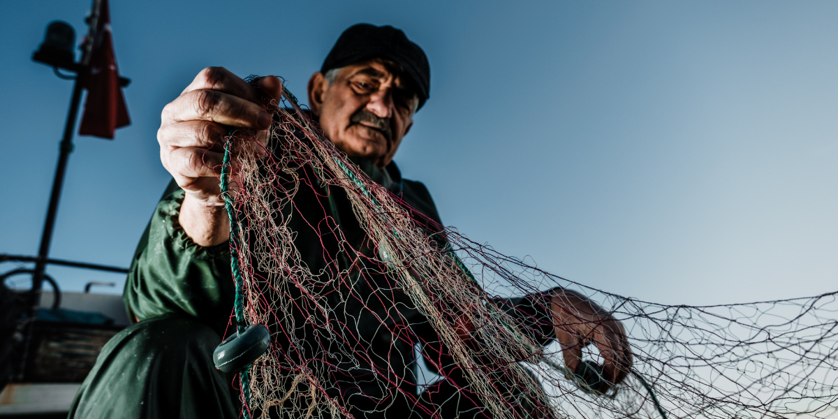 An older man is holding a large net on a boat