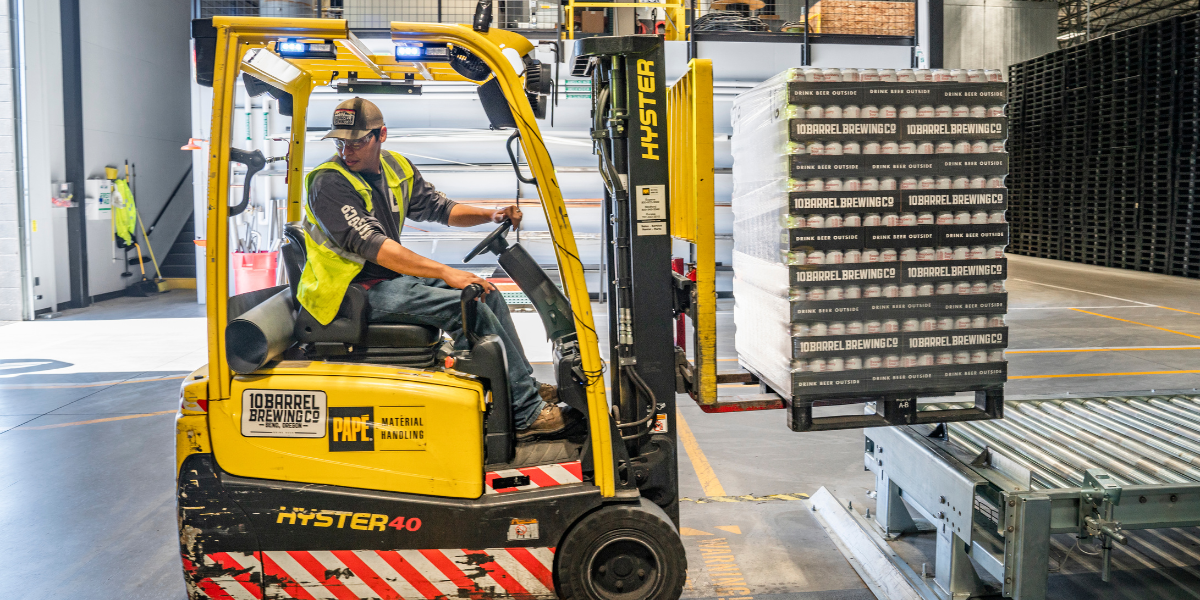 Man is looking backwards while operating a forklift with a bunch of pallets on it.