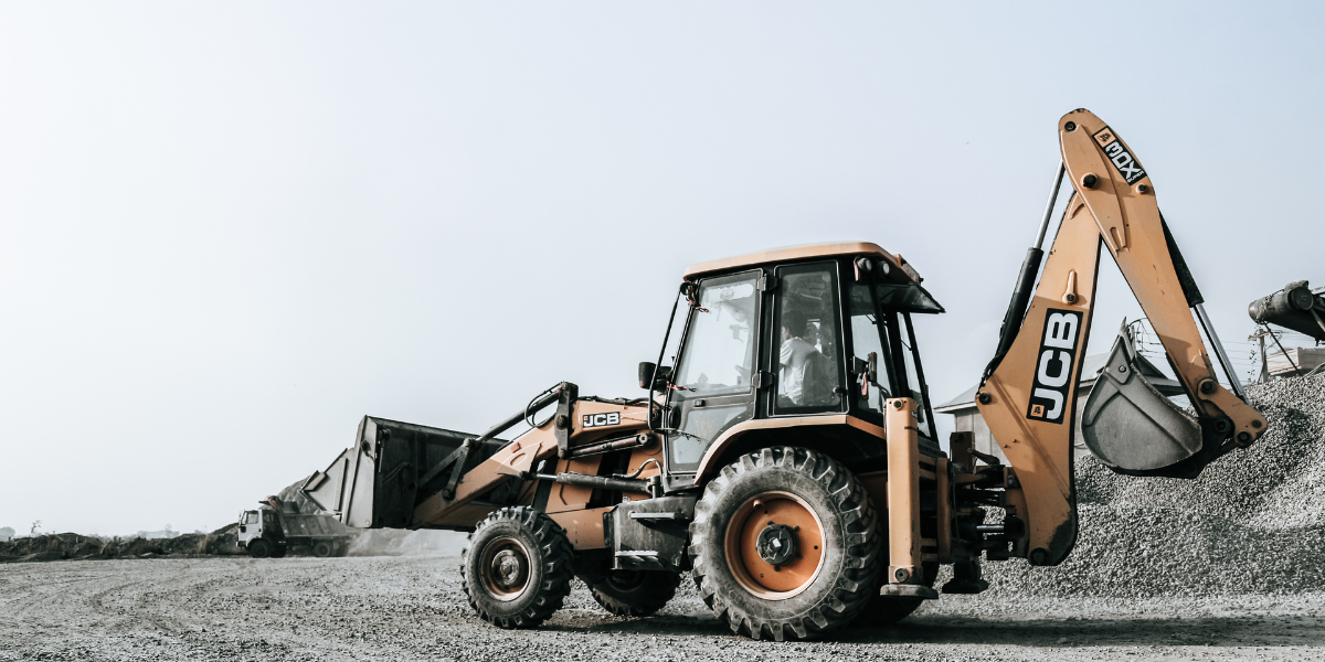 A muted photo of a tractor with backhoe attachment driving through a gravel lot