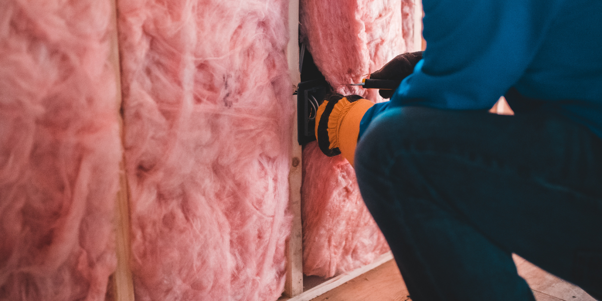 A person puts pink fiberglass insulation in between studs.