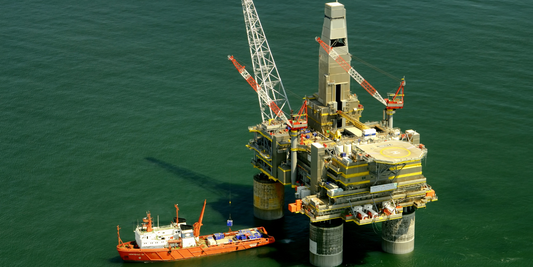 Image of oil rig in the middle of a body of water with a boat approaching