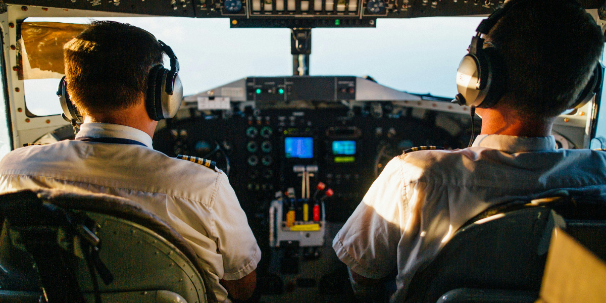 We see the cockpit of the plane with the pilot and copilot facing away from us in their seats