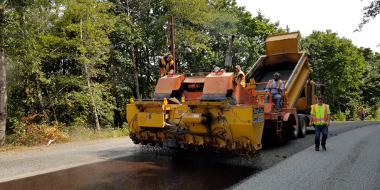 road workers lay down asphalt on a back road.