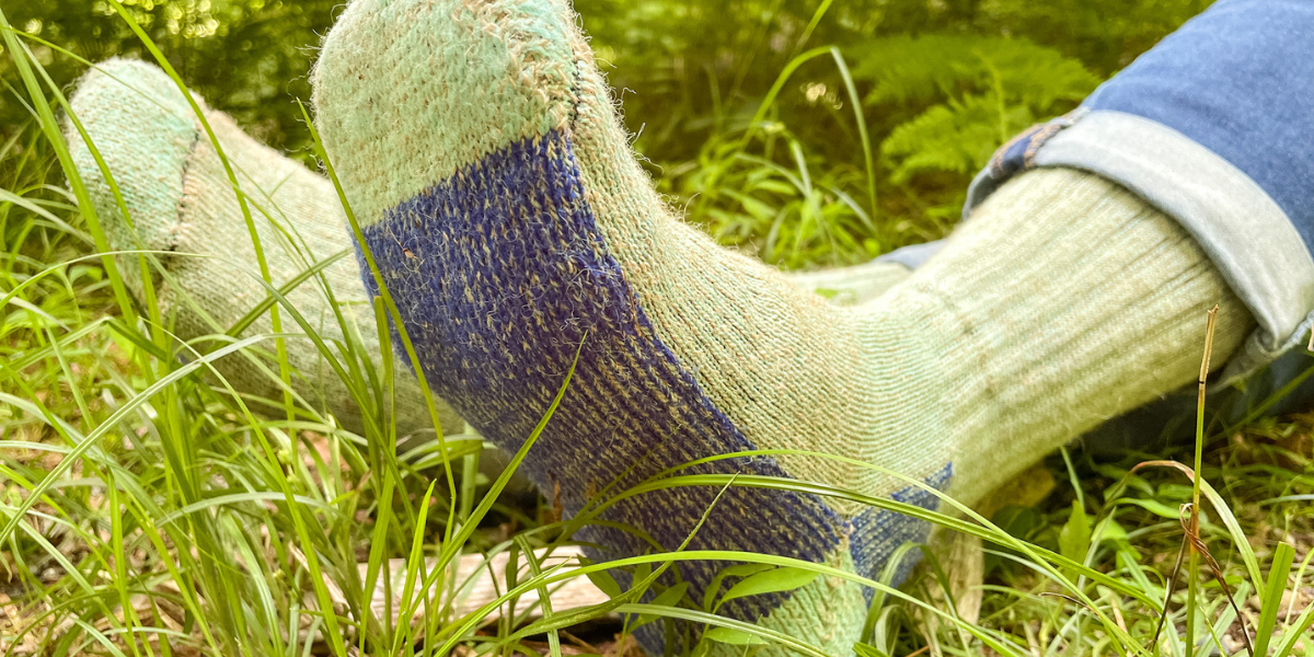 Light green alpaca socks with blue bottoms are showcased as a person sits in the grass