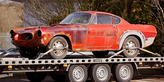 An old red muscle car is strapped onto a tow truck bed.