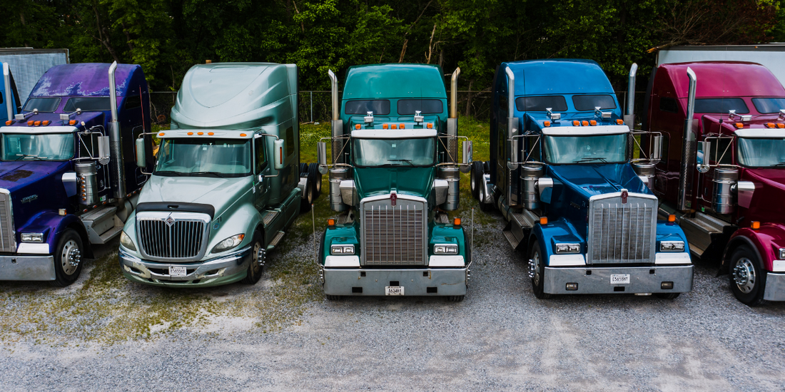 Five Trucks are lined up. They are different colors. From left to right the colors are purple, silver, emerald, royal blue, and red