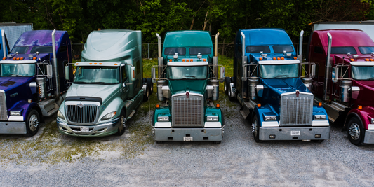 Five Trucks are lined up. They are different colors. From left to right the colors are purple, silver, emerald, royal blue, and red