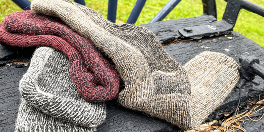 A pile of alpaca socks on a wood wagon. Silver, red, than fawn from left to right